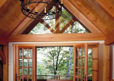 Hawk Mountain (5750) master bedroom view of doors out to small deck. Room features include timber frame, trusses and large chandelier
