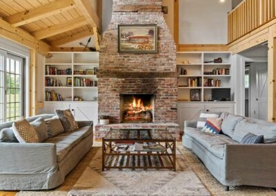 A living room in an Old Chatham Barn Home with a brick fireplace and bookshelves.