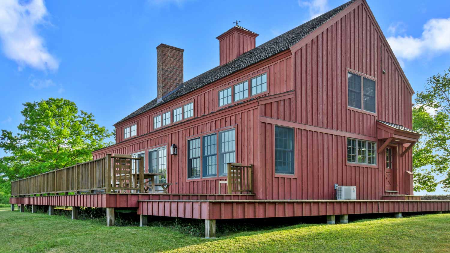 An Old Chatham barn home with a deck on a green field.